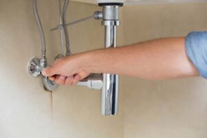 Man’s hand turning a water shut-off valve under a sink.