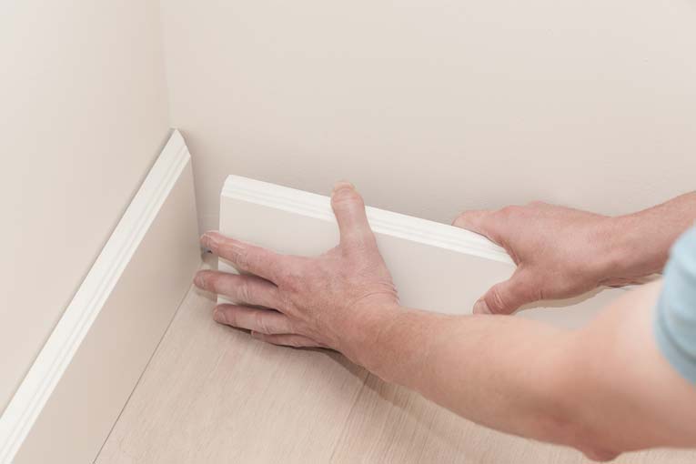 Man’s hands installing two pieces of interior trim at a room’s corner.
