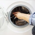 Man’s hand holding a tool, fixing the internal portion of a front-loading washing machine.