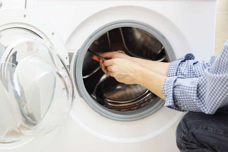 Man’s hand holding a tool, fixing the internal portion of a front-loading washing machine.