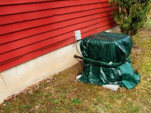 Outdoor air compressor covered in a tarp and secured with a bungee cord.