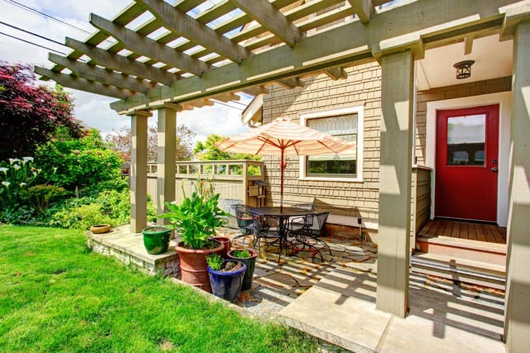 Garden stone patio beside a pergola, including a wrought iron furniture with umbrella.