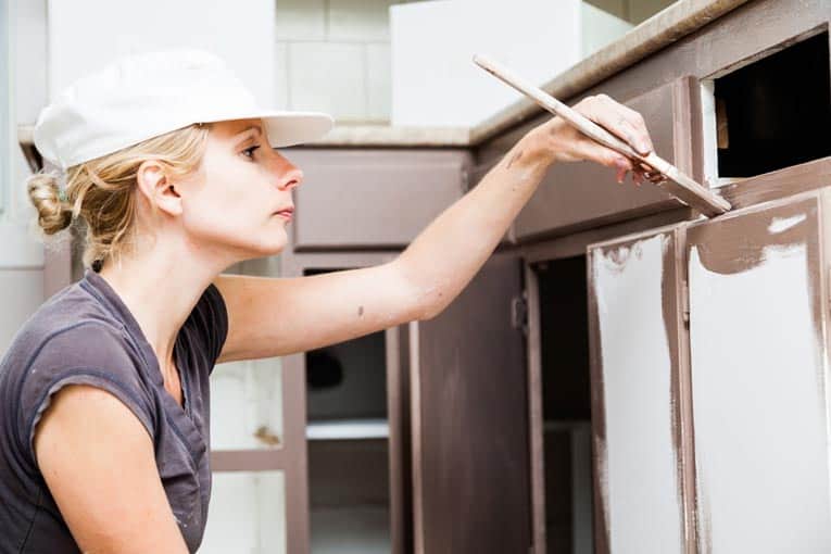 woman using paint brush to paint cabinet door