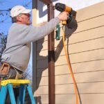 Man installing a fiber-cement wall siding with a nail gun.