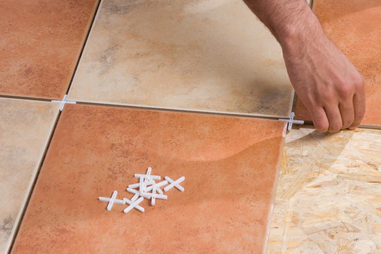 hands installing stone floor tiles, placing cross-shaped plastic spacers in grout joints to keep regular spaces between the tiles before grout is added