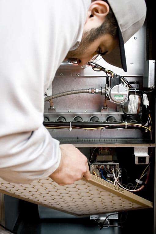 An HVAC service technician replacing the furnace filter in the air mover. 