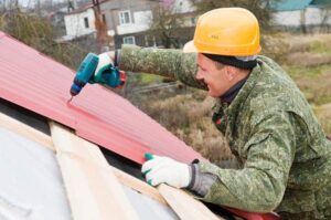 Man screwing metal roof panels over wooden battens.