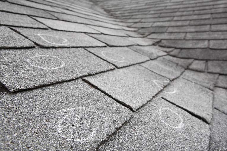 Las tejas de asfalto para techos que requieren reparación están marcadas en este techo.  Puede extender la vida útil de un techo como este con reparaciones básicas, pero finalmente deberá reemplazarse.