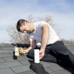 Man sealing a roof vent pipe flashing using a caulk gun.