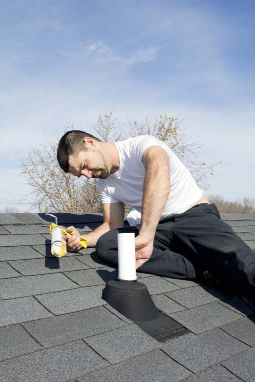 Man sealing a roof vent pipe flashing using a caulk gun.