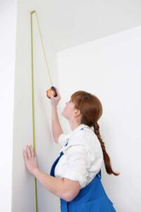 woman in overalls measuring the height of your walls with a tape measure