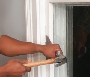 Man's hand, hammering a wide-bladed putty knife between a sash and frame.