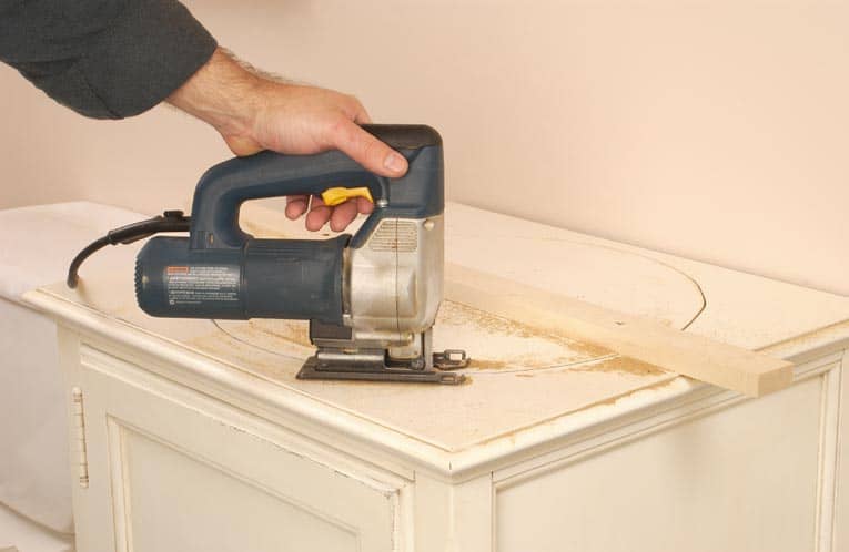 Man cutting a hole in the top of the countertop with a jig saw.