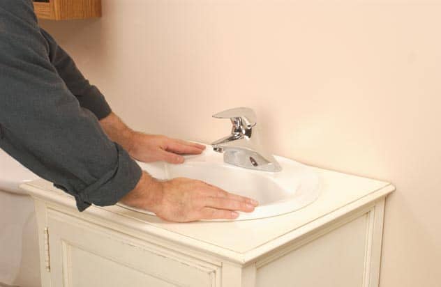 Man setting the sink in its new hole in the top of the cabinet. 