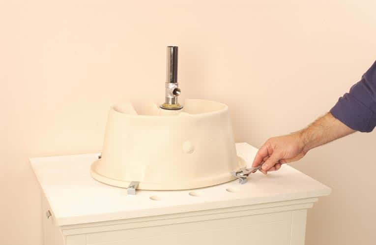 A man fastening mounting brackets to a new sink bowl, which is upside-down.