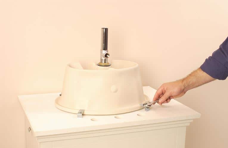 A man fastening mounting brackets to a new sink bowl, which is upside-down. 