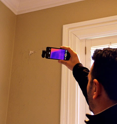 Man holding a mobile phone in front of a water damaged wall.