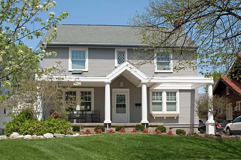 A white and grey suburban home with lush front lawn and trees.