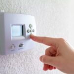 Finger pressing the down button on a programmable thermostat.