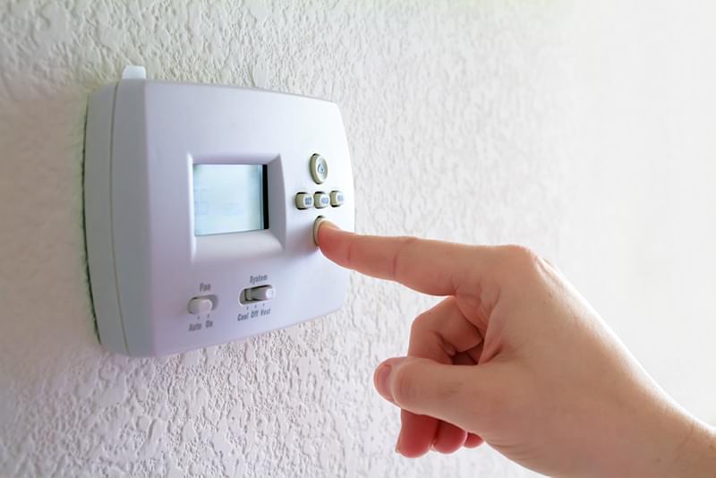 Finger pressing the down button on a programmable thermostat.