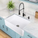 A white farmhouse sink with pull-down sprayer faucet on a marble countertop.