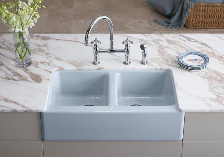 A gray double-bowl farmhouse sink on a marble countertop.