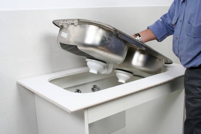 Man lifting a double-bowl sink off a white kitchen counter.