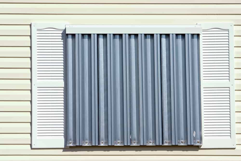 Metal hurricane shutters with track and bracket, covering a house's window opening.