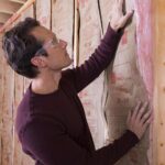 man installing fiberglass insulation between wall studs