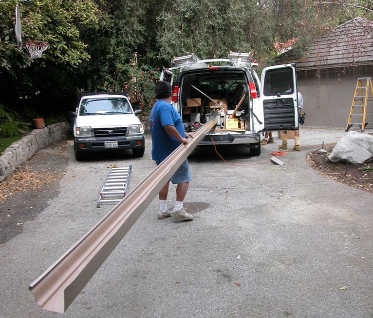 Man supporting a long gutter from an extrusion machine in a van.