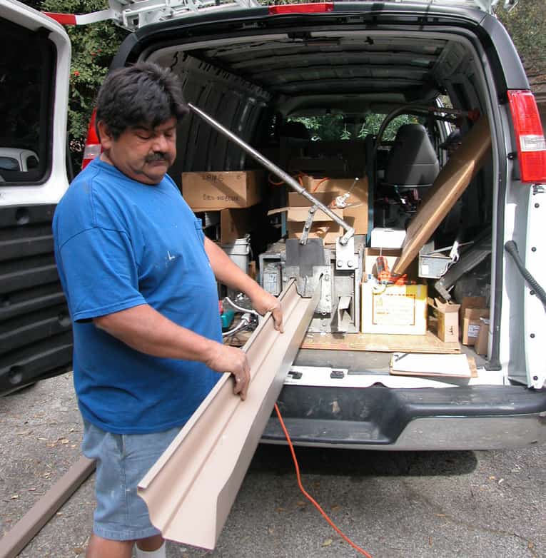 Man holding an aluminum gutter from an extrusion machine in a van.