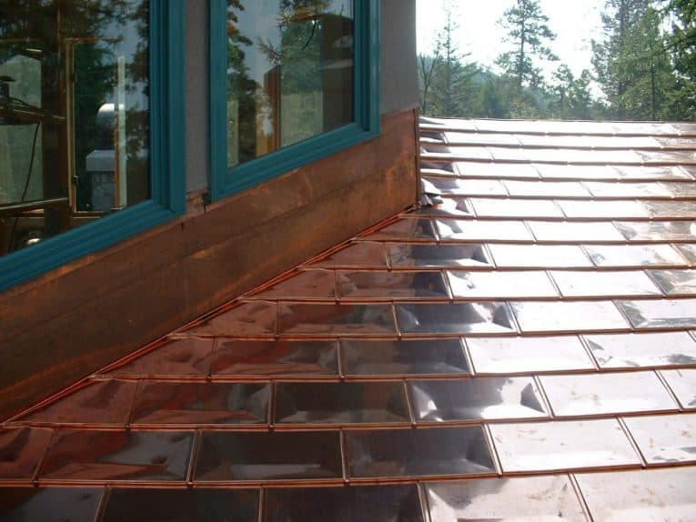 Copper shingles roofing beside a dormer window.