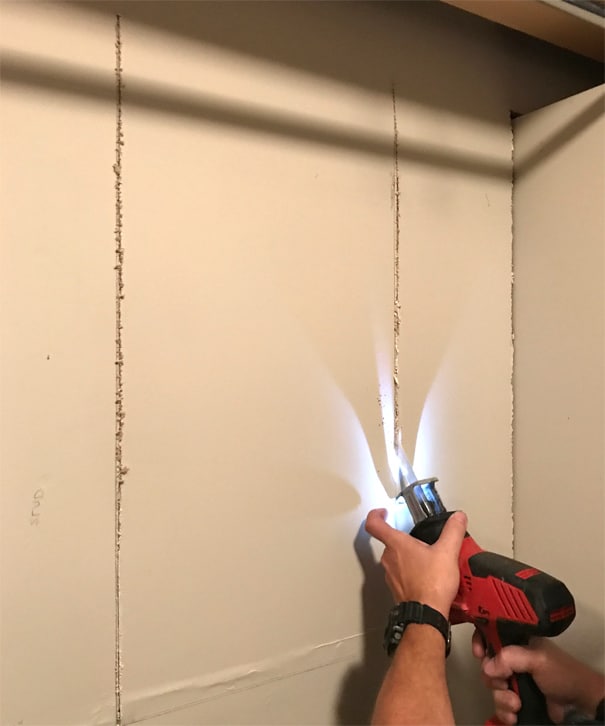 Les mains de l'homme coupant un mur à l'aide d'une scie alternative avec lumière LED.