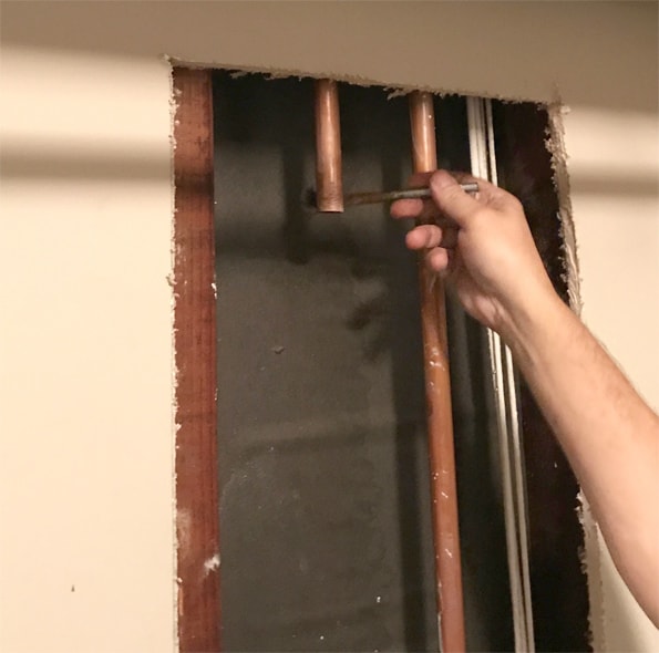 Man’s hand painting the pipe’s cut end behind a cut-away wall.