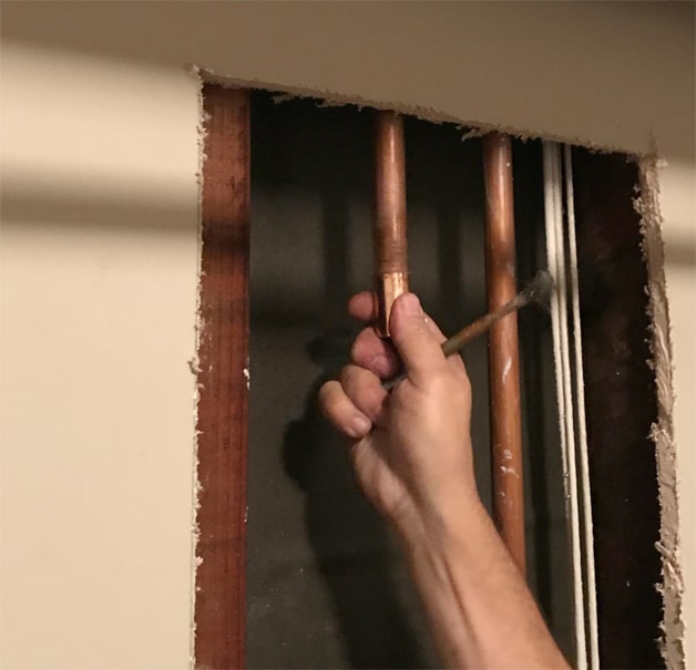 Man’s hand sliding a coupling onto a pipe behind a cut-away wall.