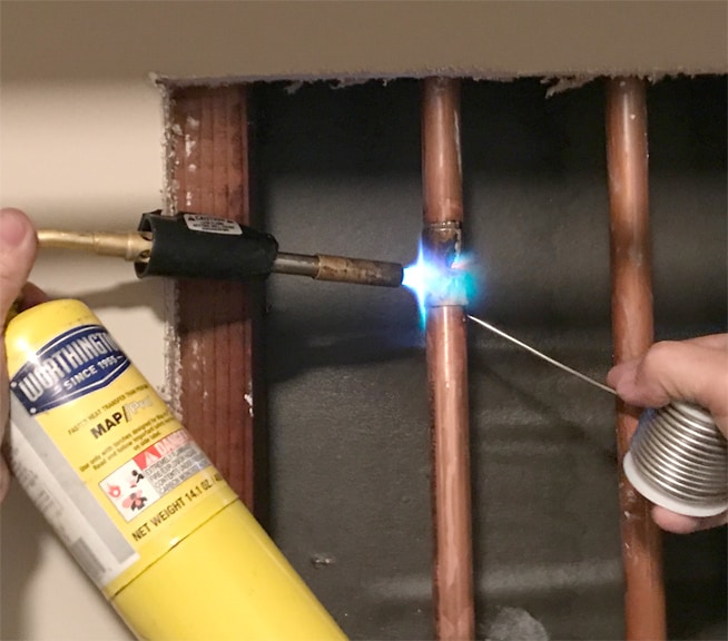 Man’s hands soldering a top coupling with a Worthington torch kit.