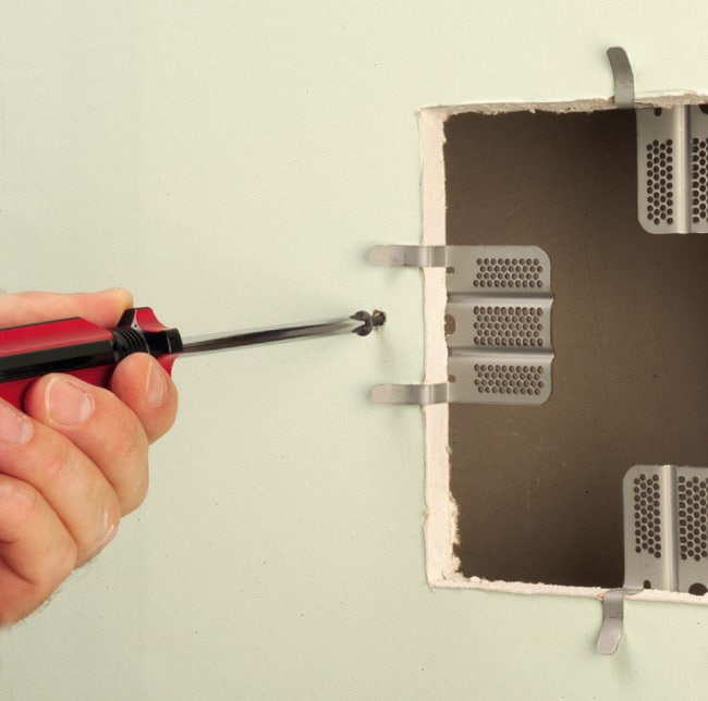 Using screwdriver to fasten drywall repair clips to four sides of cutout in drywall