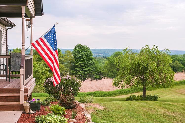 An American flag hung on a house's porch including a front yard. 