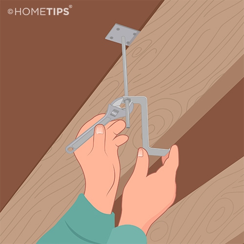 Hands using a wrench to tighten the nut on a Squeak-Ender device between the subfloor and a joist.