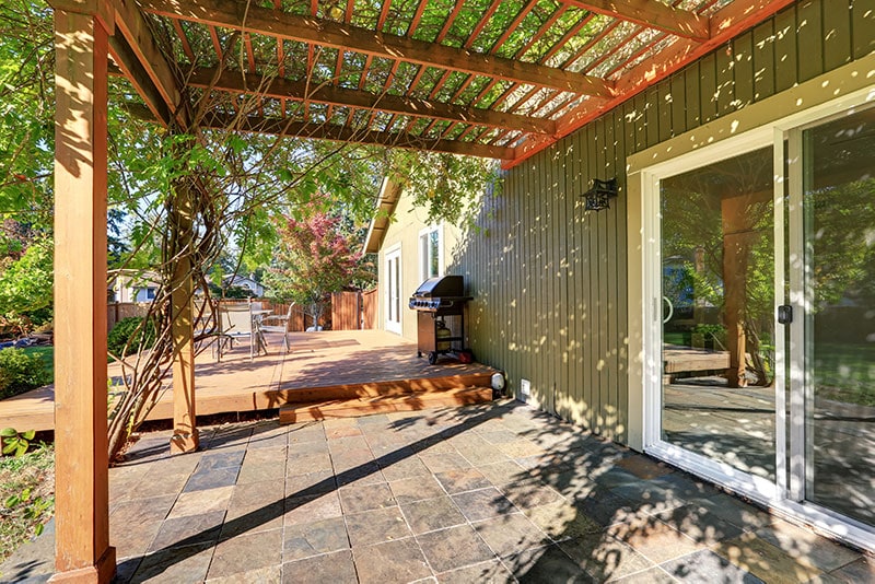 Wooden pergola attached to a house above a tile porch.