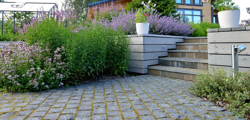 Cobblestones driveway and flagstone stairs surrounded by a vibrant garden.