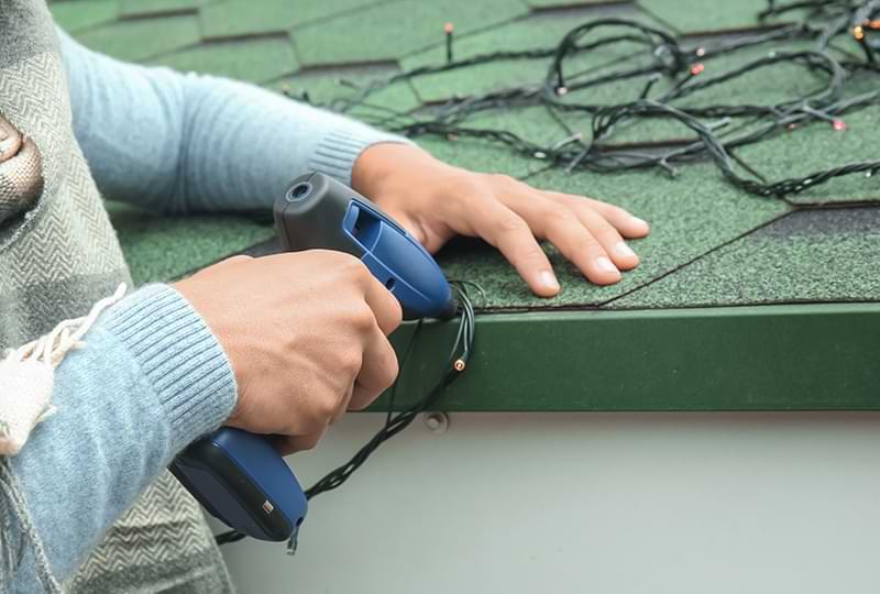 Hands using a screw gun to hang led Christmas lights on a roof.