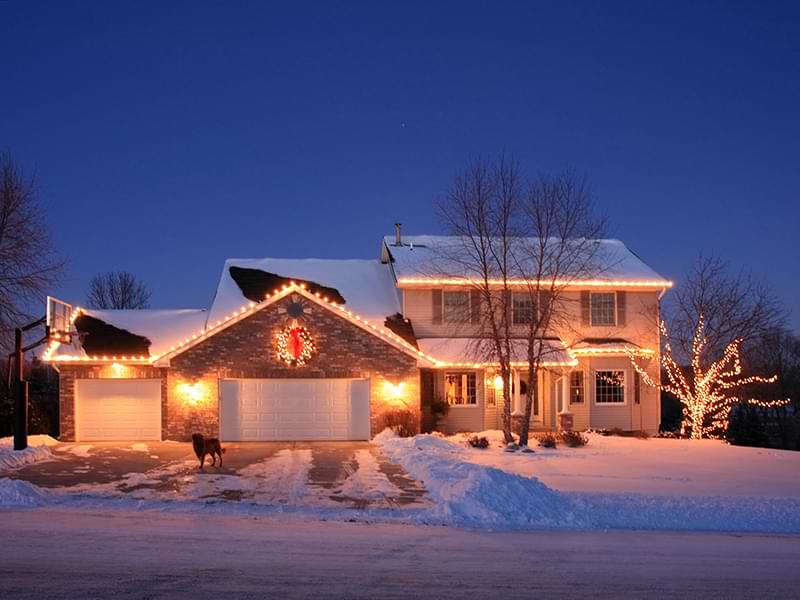 A house with the warm glow of holiday lights in the snow.