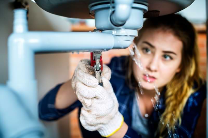 A woman working below a leaking sink